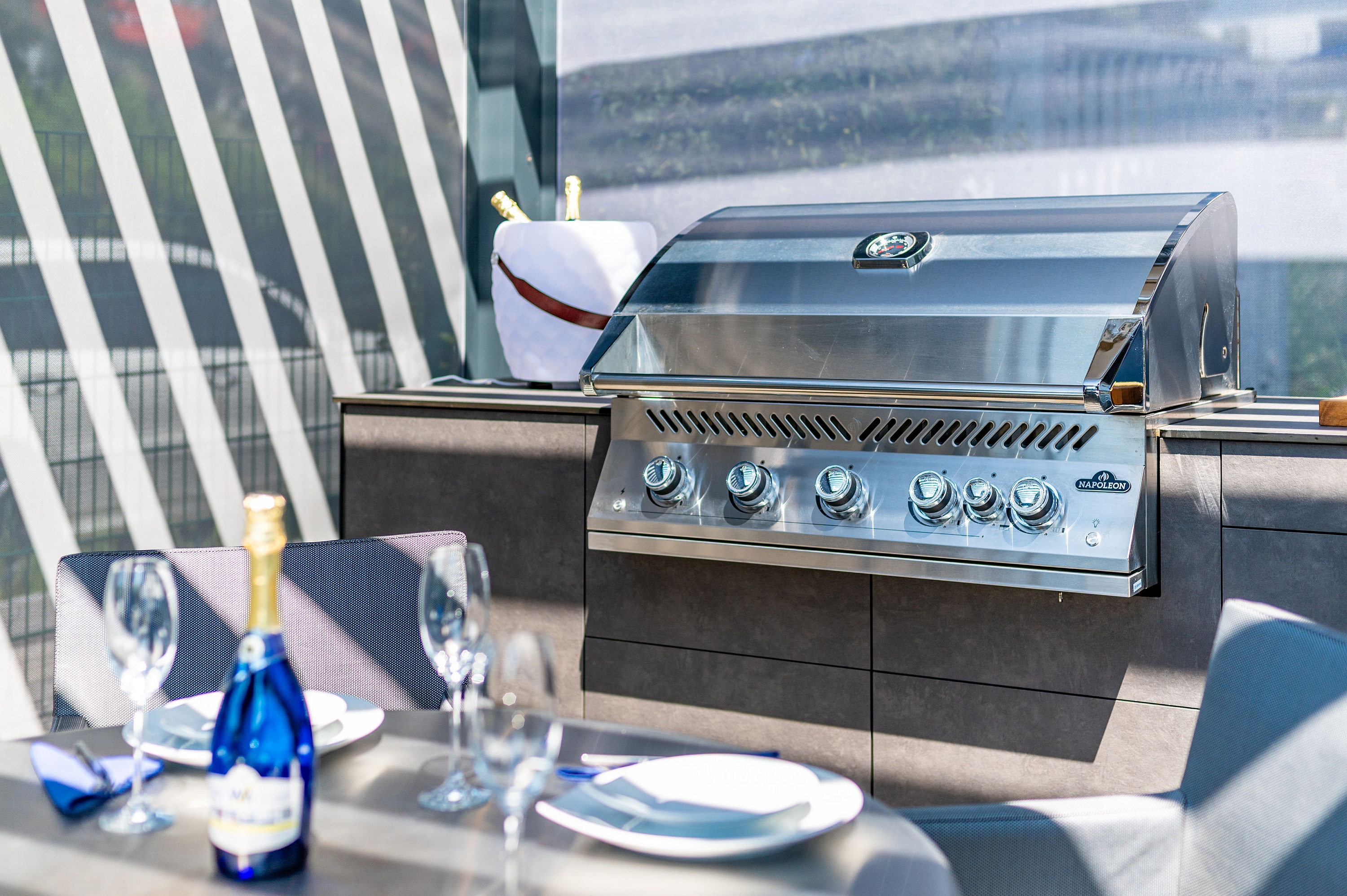 Verchromter Grill in Küchenzeile hinter Esstisch mit Sektflasche