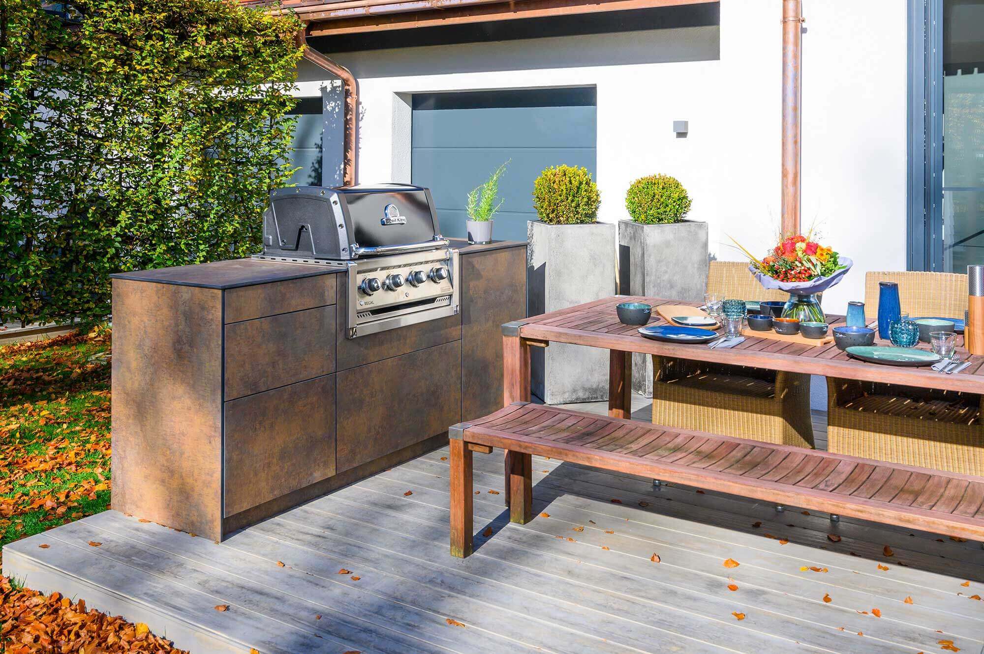Küchenzeile mit Grill auf Terrasse neben Esstisch mit Bank