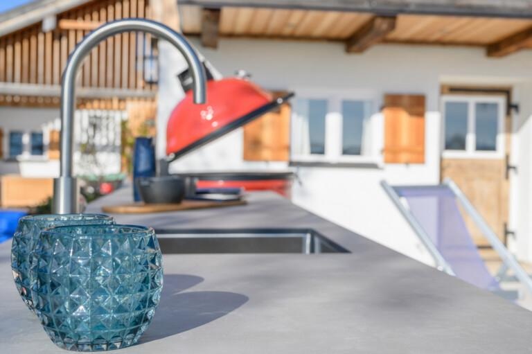 Küchenzeile draußen, im Vordergrund Trinkgläser und Armatur mit Spüle