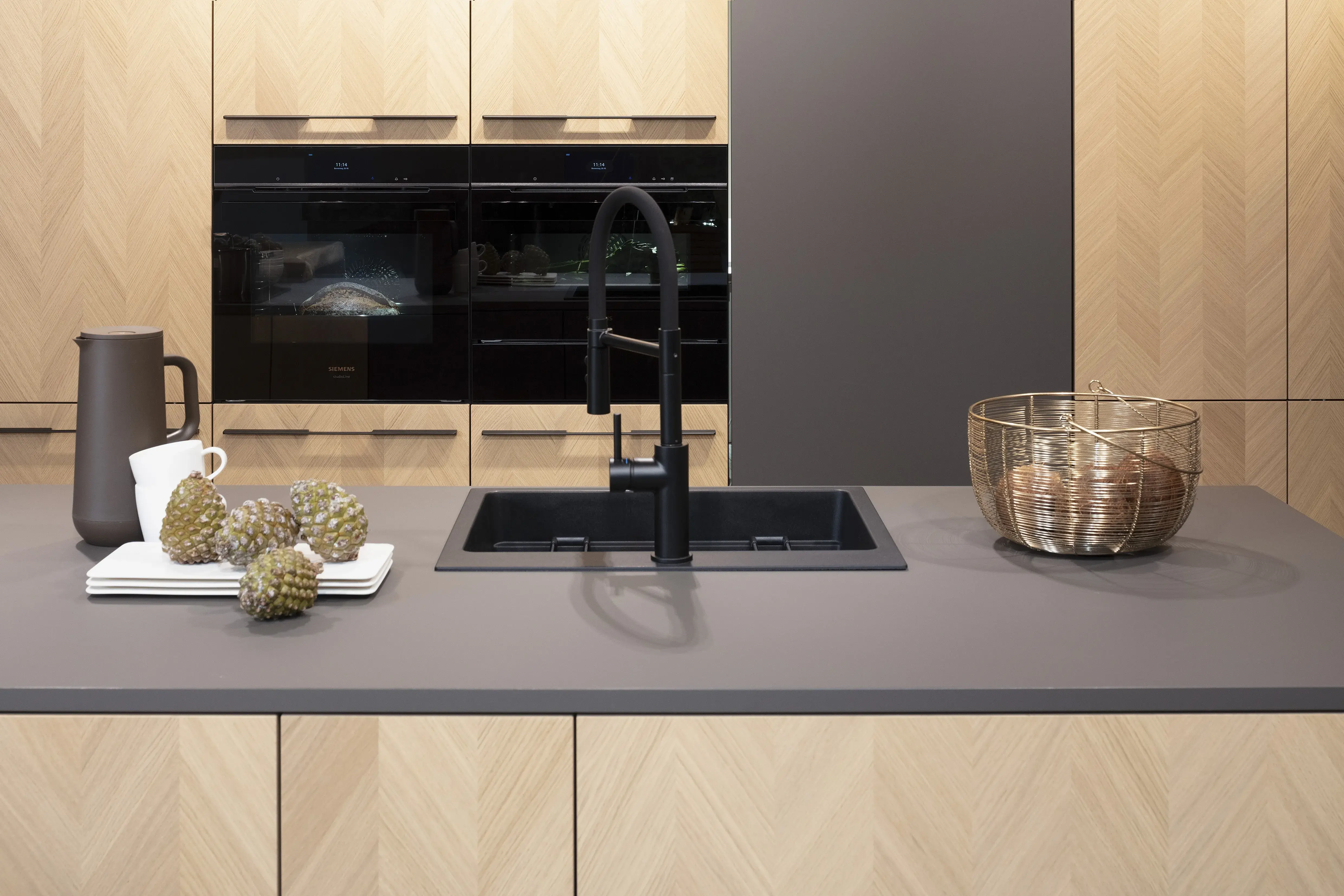 Front: Intarsia Gavi Eiche Furnier Resopal Brown Powder supermatt Korpus Schwarz APL: Resopal Brown Powder supermatt Geräte: Siemens Studio Line Spüle und Armatur: Blanco   Features: Front Echtholz Fischgrät-Optik, Kombination Echtholz und Resopal supermatt, Einbautür in Frontmaterial Resopal, Küchentheke Massivholz, APL = Korpusfarbe = Frontmaterial, Kombination Griffleiste und grifflos, Korpus in Frontmaterial, Wärmeschublade, Spüle und Armatur Schwarz, Besteckeinsatz. 